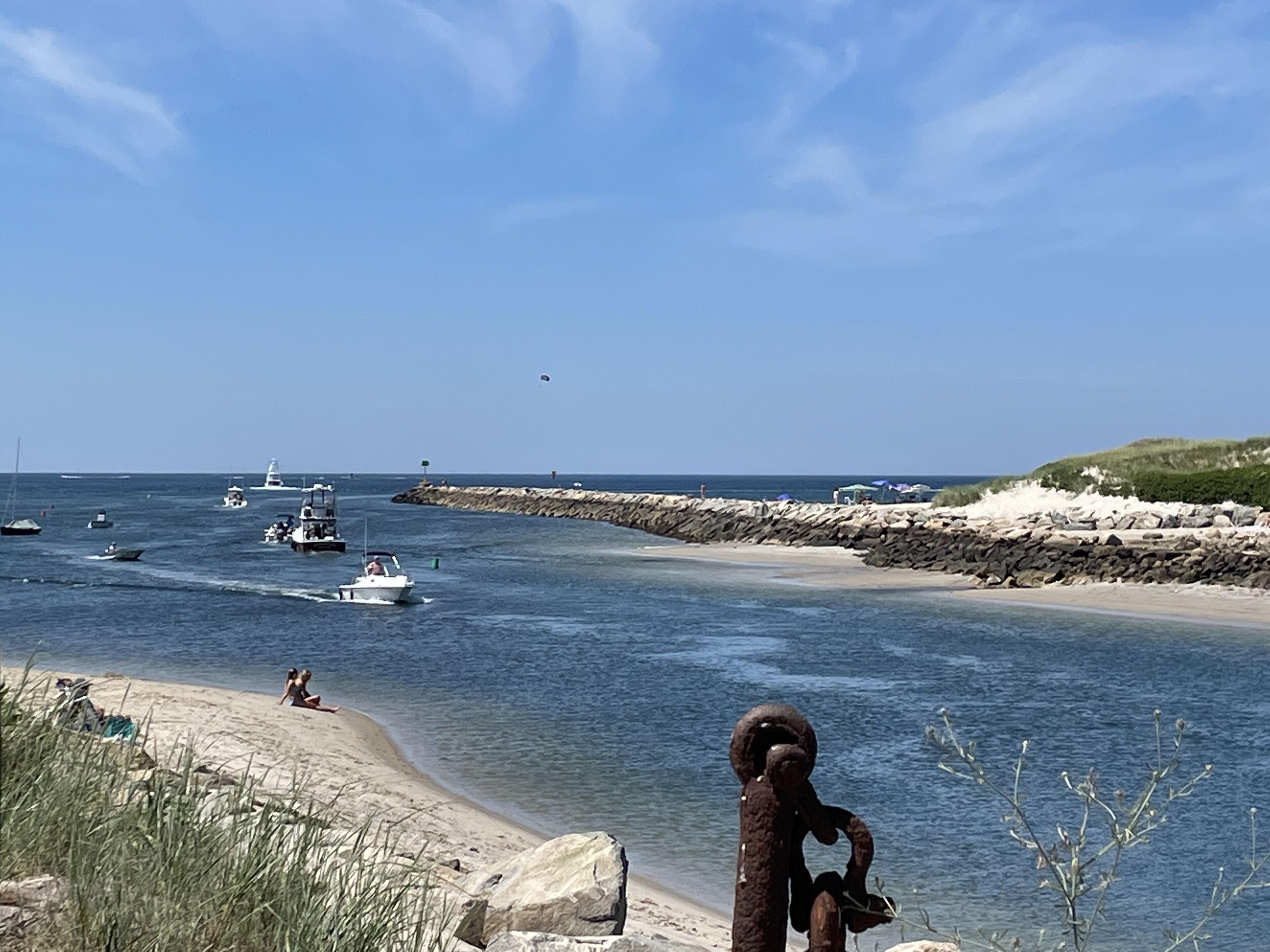 Un paysage côtier avec des bateaux sur l’eau, une plage de sable et une digue rocheuse.