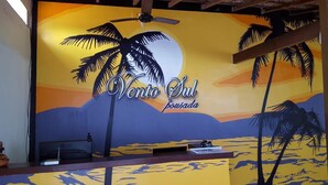 A reception desk with a tropical mural, a ceiling fan, and a laptop. - Pousada Vento Sul (Angra dos Reis)