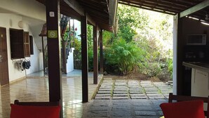 A covered outdoor seating area with stone flooring, wooden pillars, and red chairs. - Pousada Vento Sul (Angra dos Reis)