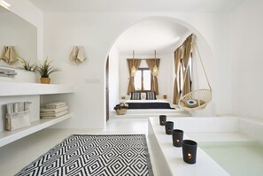 A modern bathroom with a large mirror, white shelves with towels, a patterned rug, and candles. - Le Blanc Suite Santorini  Luxury and Family Friendly (Mesaria)