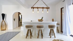A modern kitchen with a white island, three woven stools, and a hanging light fixture. - Le Blanc Suite Santorini  Luxury and Family Friendly (Mesaria)