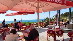 Un área de estar al aire libre con sillas y mesas rojas, sombrillas y vistas al mar.