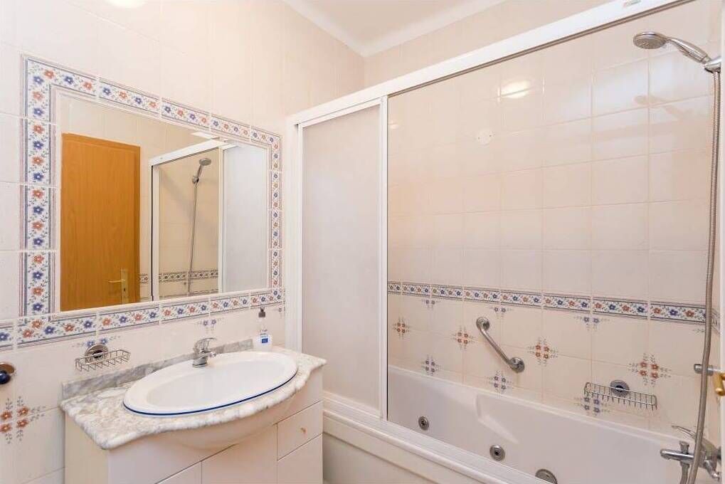 Une salle de bain avec un lavabo blanc, un miroir et une cabine de douche.