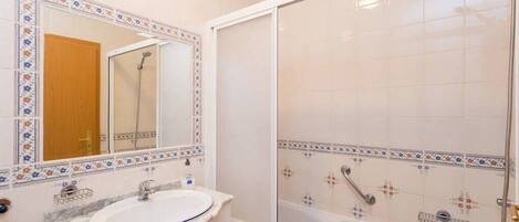 A bathroom with a white sink, mirror, and shower enclosure.