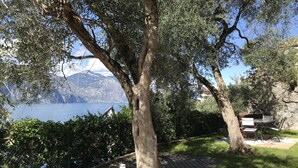 A patio area with a stone pathway, a metal table and chairs, and a view of a lake with mountains in the background.