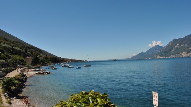 A coastal view with boats, a clear sky, and mountains in the background.