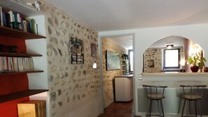 A kitchen with a stone wall, a refrigerator, and a bar area with stools. - DROME-LIMIT VAUCLUSE-GÎTE WITH SWIMMING POOL - PANORAMIC VIEW (Vinsobres)