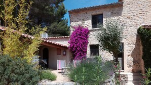 A stone building with a tiled roof, surrounded by a garden with various plants and a pink flowering bush. - DROME-LIMIT VAUCLUSE-GÎTE WITH SWIMMING POOL - PANORAMIC VIEW (Vinsobres)