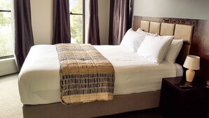 A neatly made bed with white linens and a patterned throw blanket, a wooden headboard, and a bedside lamp on a small wooden nightstand.