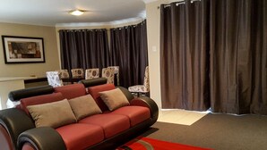 A living room with a red sofa, patterned chairs, a red carpet, and dark curtains.