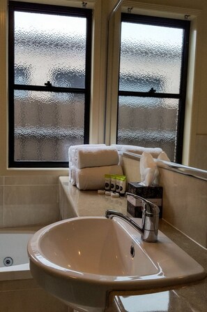 A bathroom with a bathtub, a sink, and a window with frosted glass. - Atricom Apartments Australia (Stanthorpe)