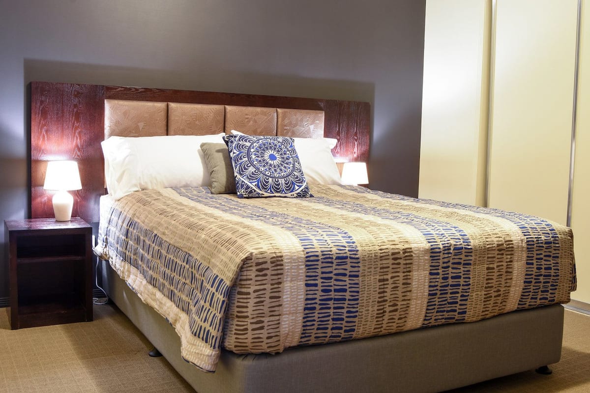 A neatly made bed with a patterned bedspread, two bedside lamps, and a wooden headboard.
