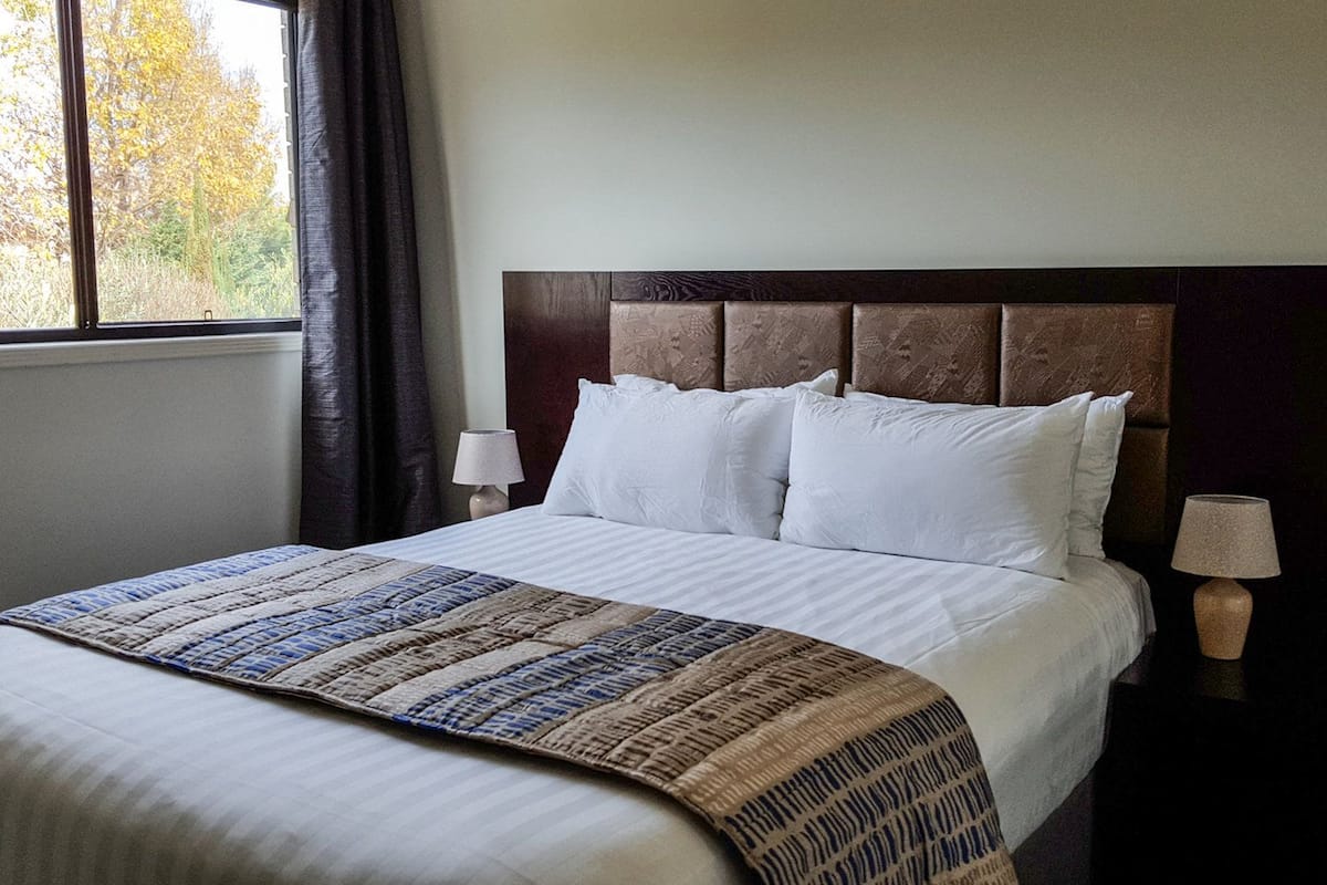A neatly made bed with a patterned bedspread, a dark headboard, and two bedside lamps.