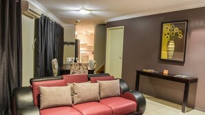A living room with a red leather sofa, a black and red armchair, a small table with books, a framed artwork, and a red and black rug.