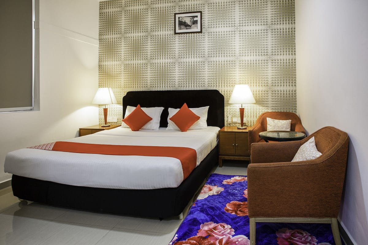 Une chambre d’hôtel comprenant un lit, deux tables de chevet, une chaise, un tapis décoratif et un mur à texture.