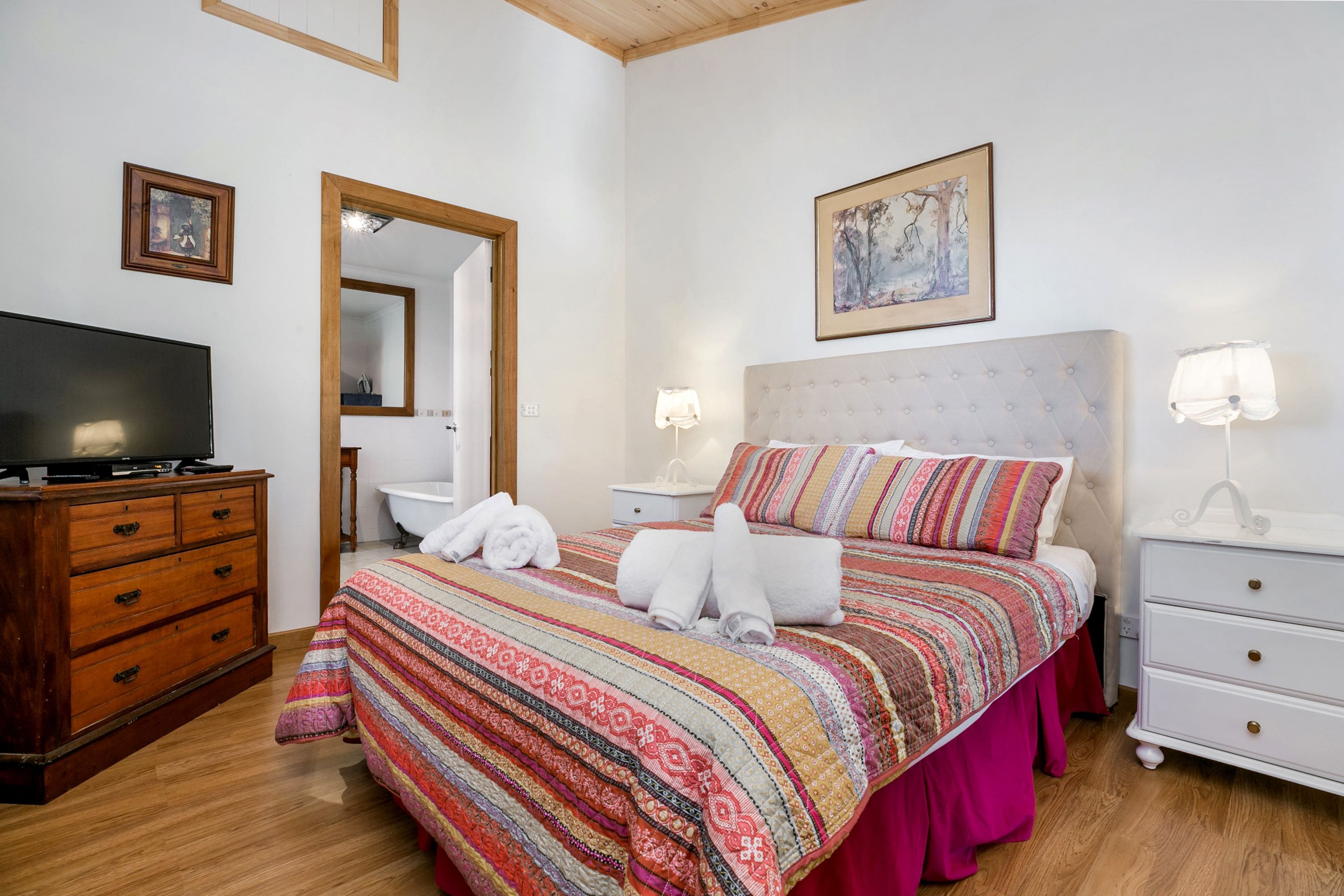 A bedroom with a bed, a television, a dresser, a nightstand, and a mirror.