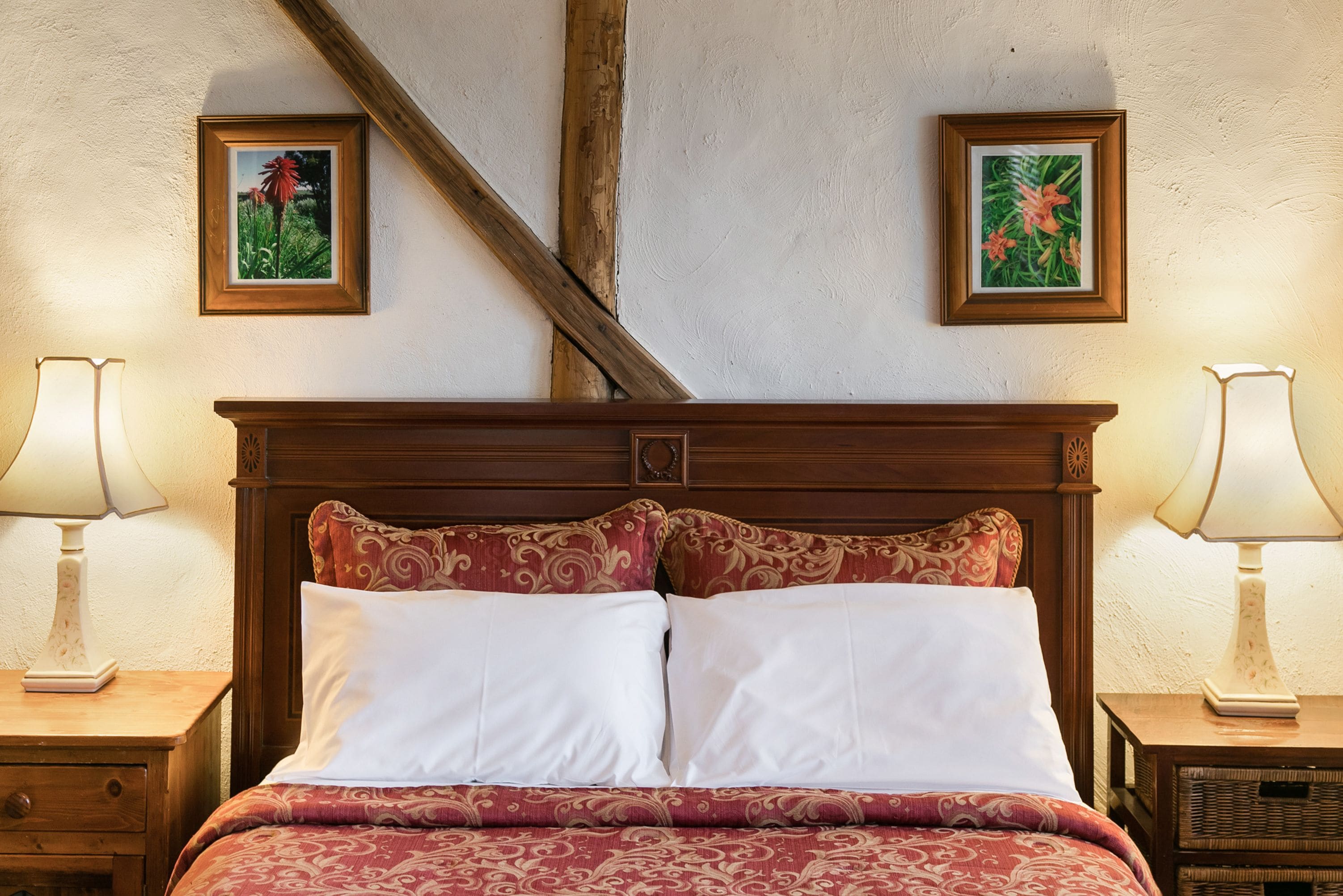 A bedroom with a wooden headboard, two bedside tables with lamps, and two framed floral pictures on the wall.