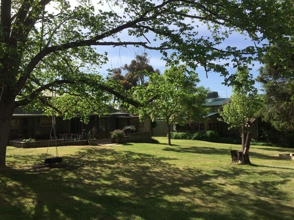 Un patio con césped, un conjunto de columpios y un edificio con porche.