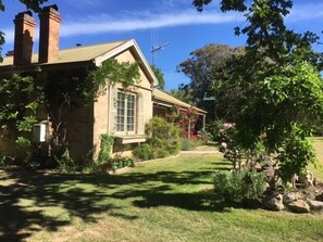 A house with a sloped roof, a chimney, and a window. There is a garden with grass, a tree, and a rock formation. - Taradale House Estate (Taradale)