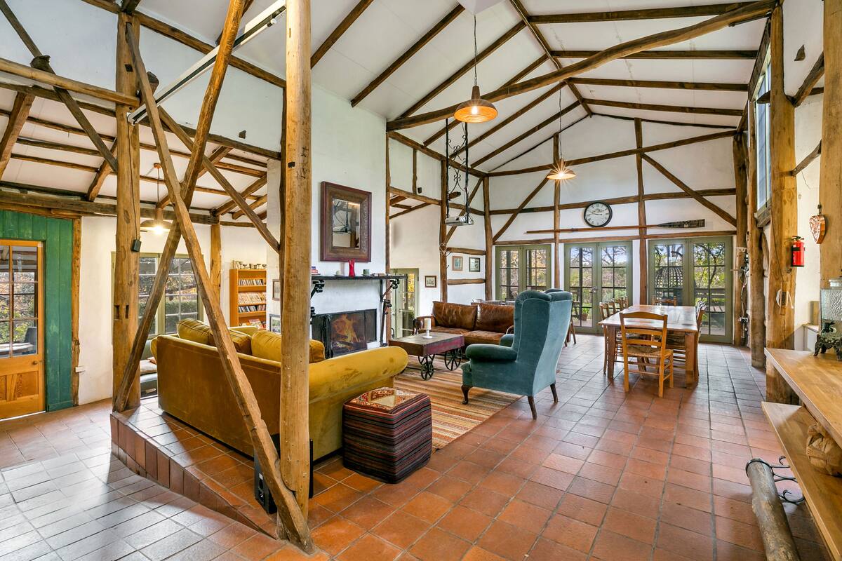 Un interior rústico con vigas de madera a la vista, chimenea, comedor y sofá.