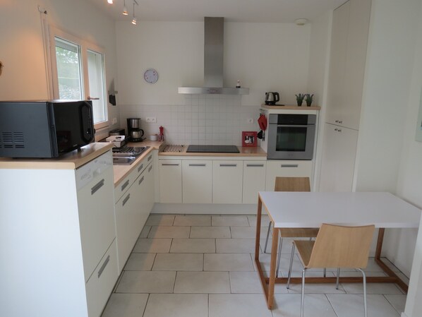 A modern kitchen with white cabinets, a microwave, a stove, and a sink. There is a dining table with chairs. - Private contemporary two bedroom house between Santenay and Nolay (Paris-L'hôpital)