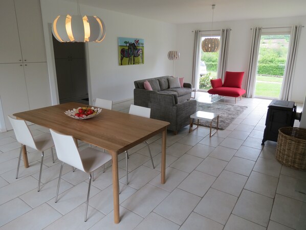 A modern living room with a dining area, a grey sofa, a red chair, and a large window with curtains.