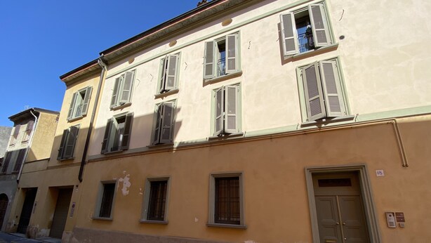 Un edificio con varias ventanas y una puerta, algunas con contraventanas, y el número '18' a la vista.