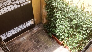 Un patio con suelo de baldosas, una verja metálica y un seto verde frondoso.