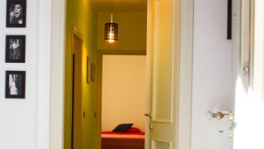 Un pasillo con una cama al fondo, una puerta a la derecha y una lámpara arriba.