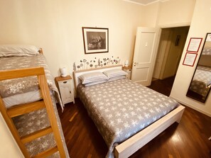 Een slaapkamer met een groot bed, een kleiner bed, een nachtkastje, een kledingkast en een deur naar een andere kamer.