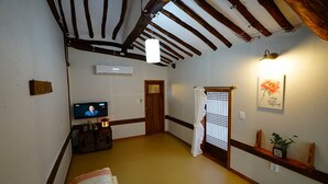 Ein traditioneller japanischer Raum mit Tatami-Boden, einem Fernseher, einem Holzregal mit einer Uhr und einer Schiebetür.