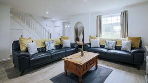 A living room with a black leather sofa, wooden coffee table, and a staircase. - Atlantic Reach Cottage, Newquay.  Large 4 bed villa with leisure services & WiFi (Newquay)