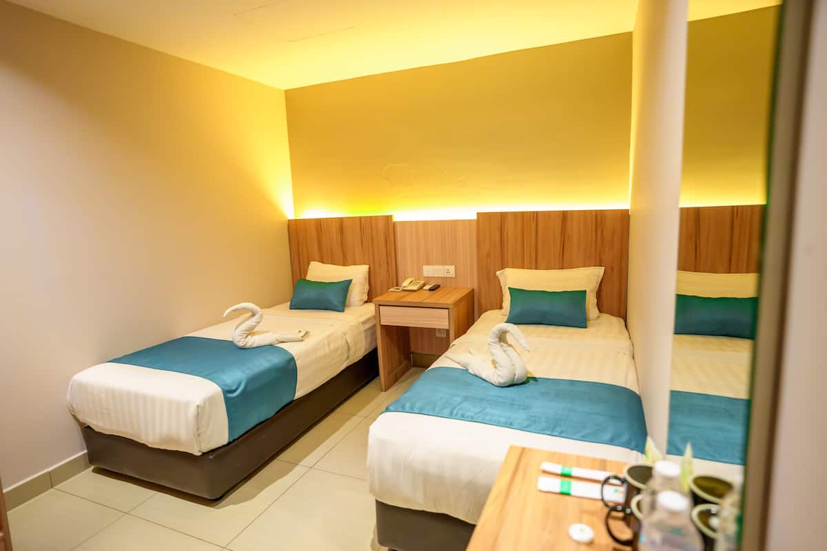 Una habitación de hotel con dos camas individuales, cada una con cubrecama azul y almohadas blancas, y una mesita de noche de madera entre ellas.
