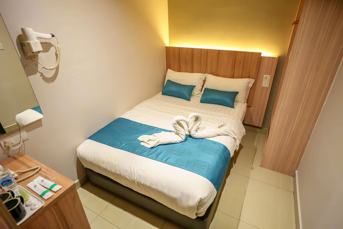 Habitación de hotel con cama, mesita de noche con secador de pelo y espejo.