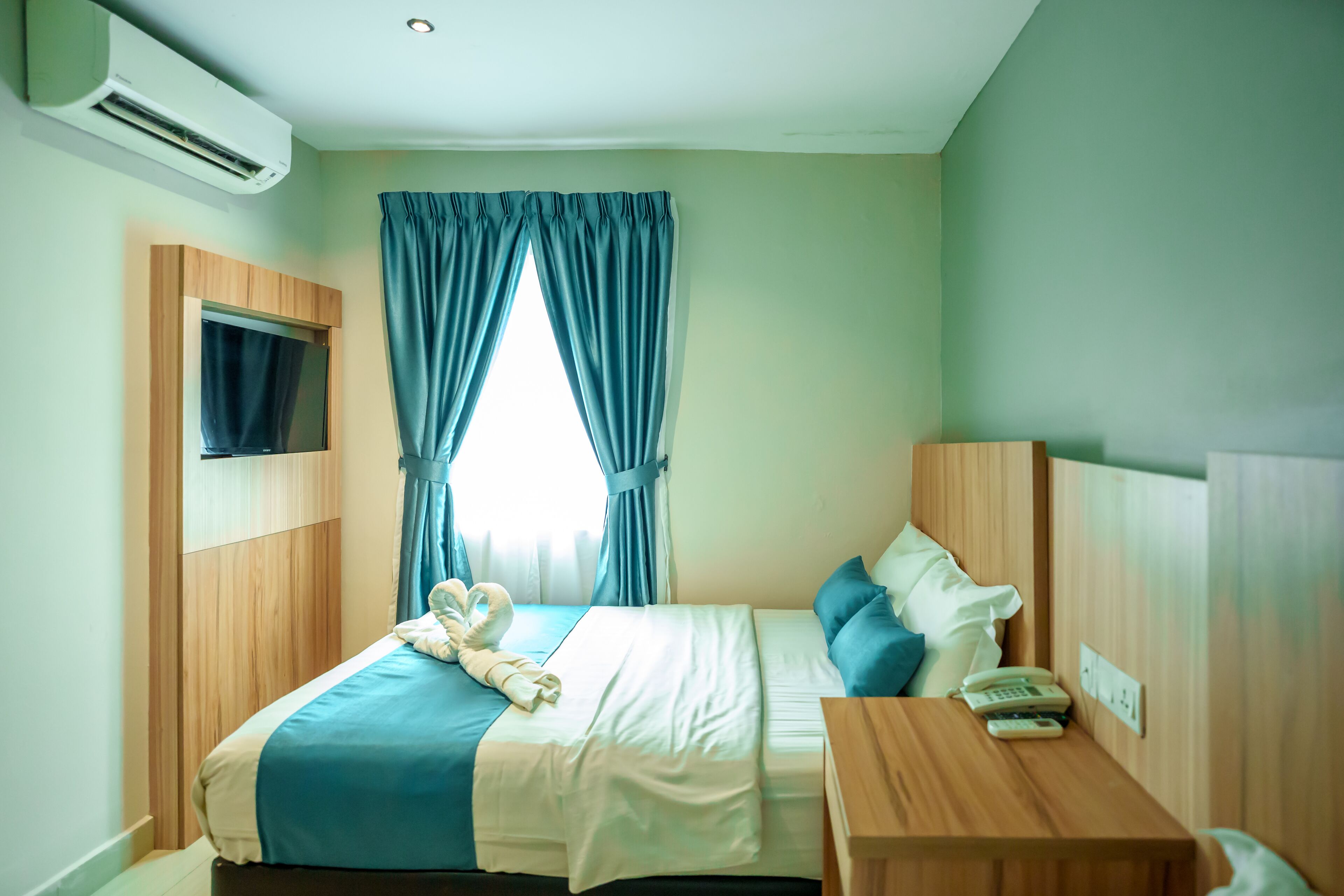 A hotel room with a bed, bedside table, and a TV mounted on the wall.