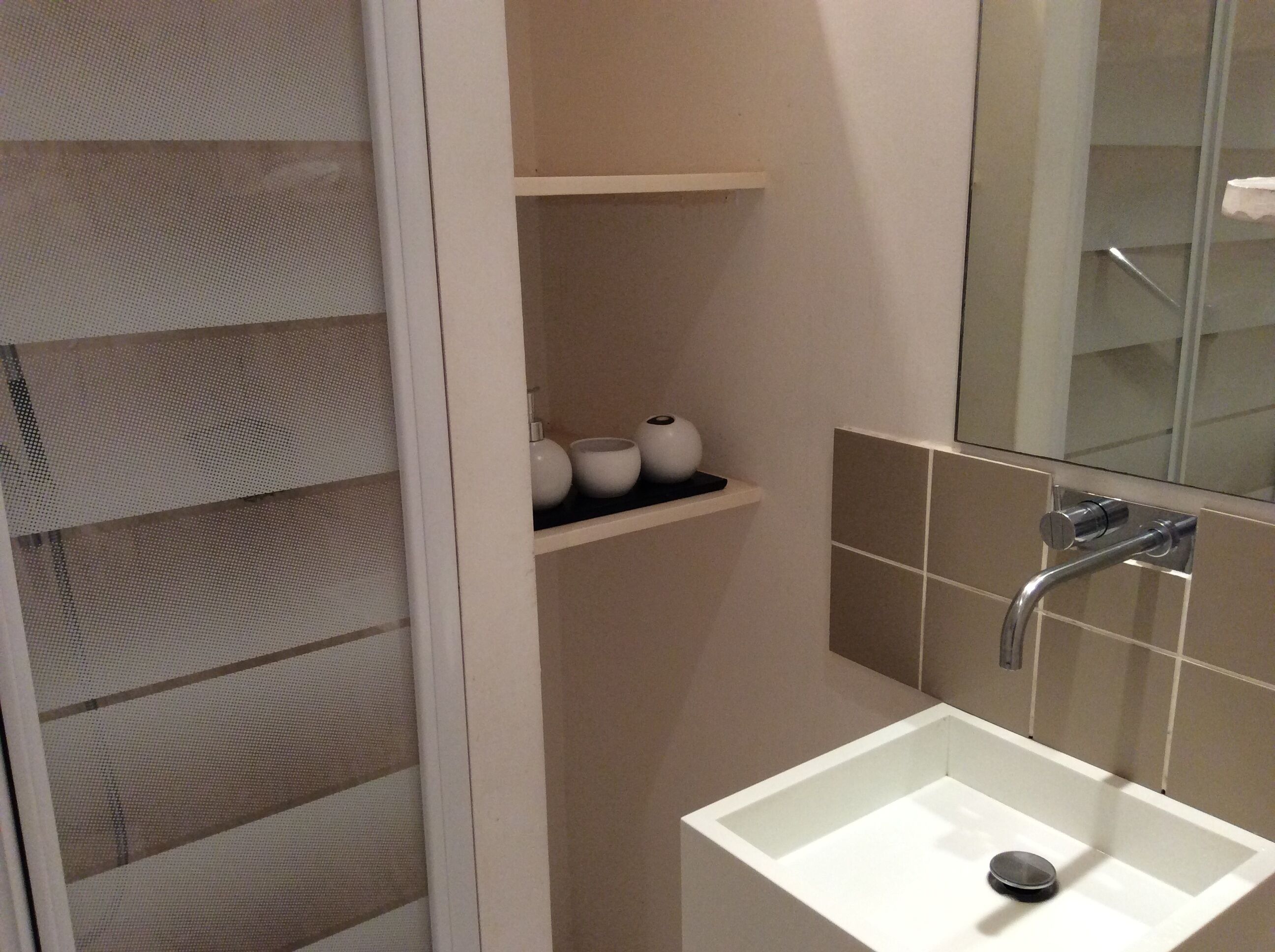 A bathroom with a white sink, a mirror, and a shelf with toiletries.