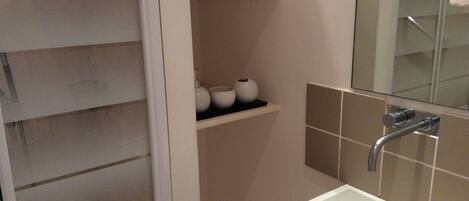A bathroom with a white sink, a mirror, and a shelf with toiletries.
