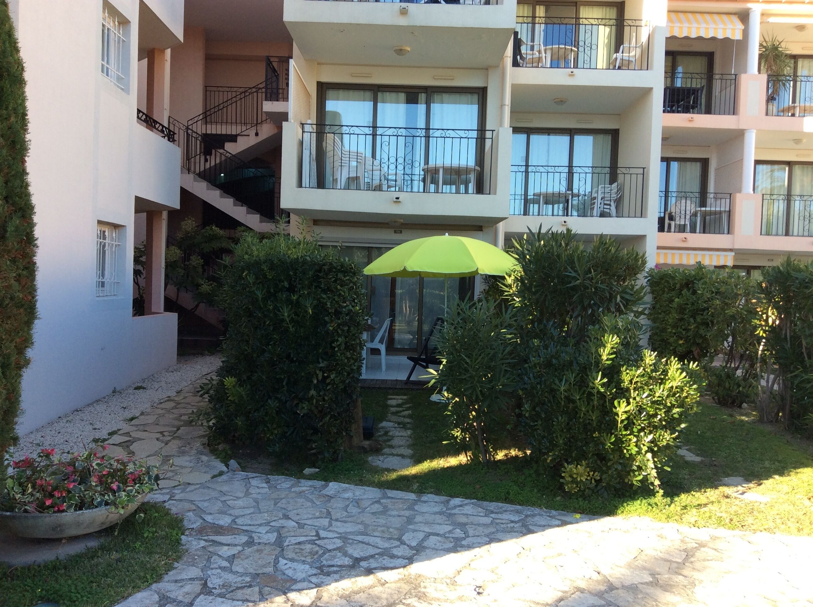 Un immeuble résidentiel à plusieurs étages, doté de balcons, d’un chemin pavé en pierre et d’un parasol vert.