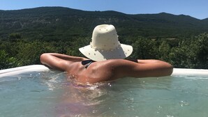 Una persona si rilassa in una vasca idromassaggio con vista su dolci colline verdi.