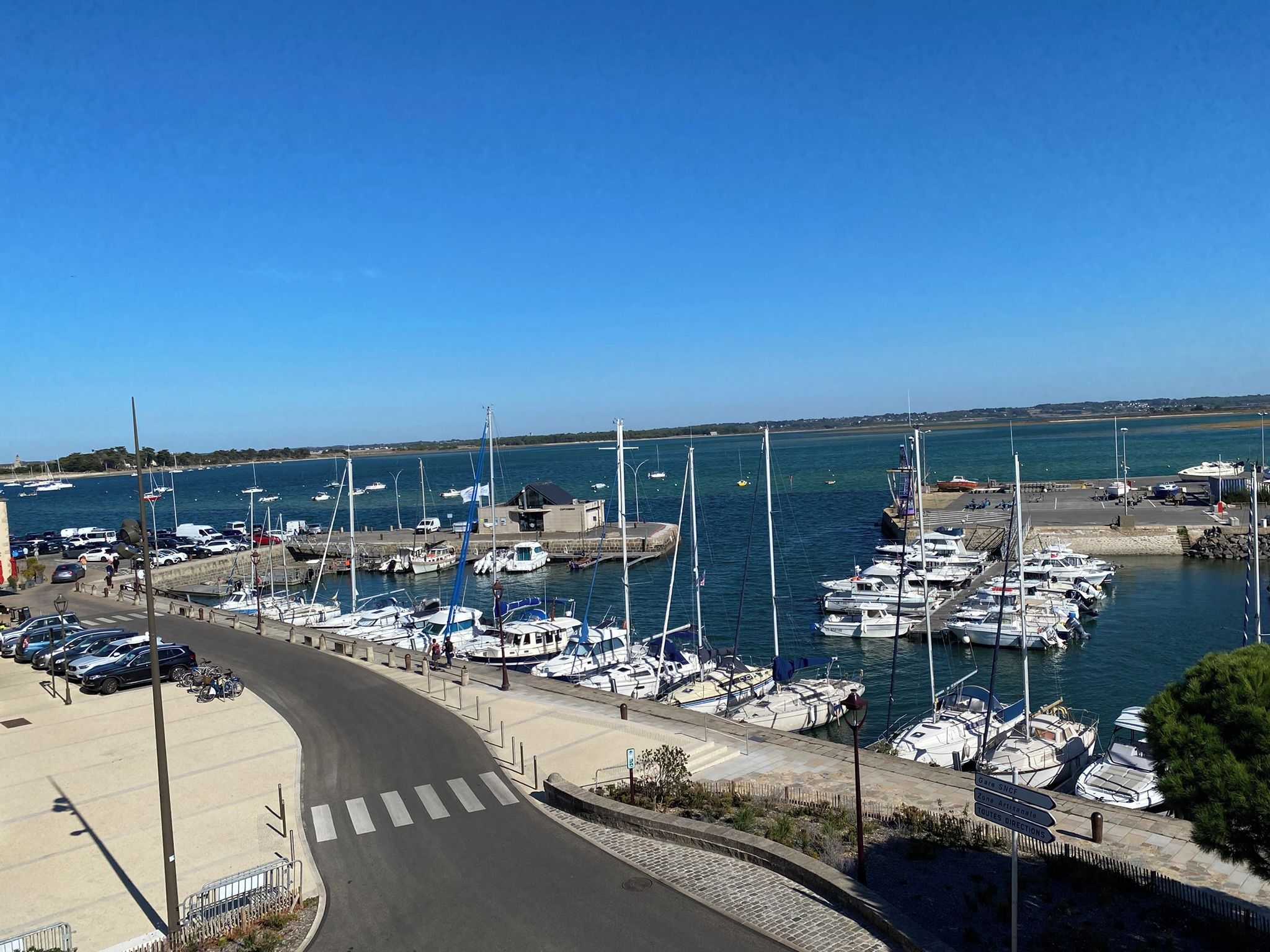 A marina with boats docked, a clear sky, and a road curving around the harbor.