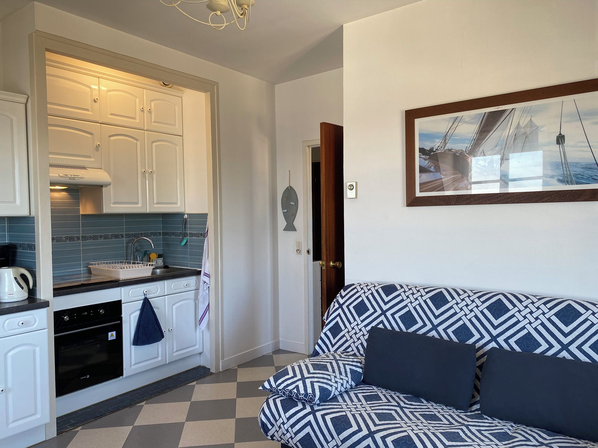 A compact living space with a kitchenette, a sofa with patterned cushions, and a framed picture on the wall.