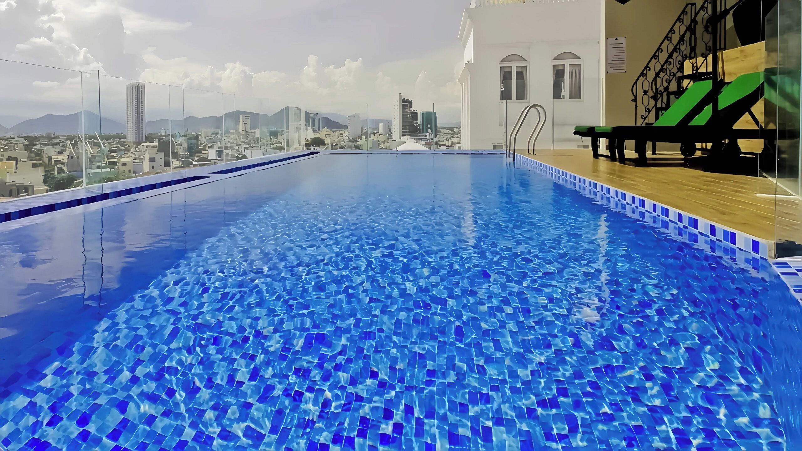 Une piscine sur le toit avec vue sur la ville, une petite table au bord de la piscine et une chaise verte.