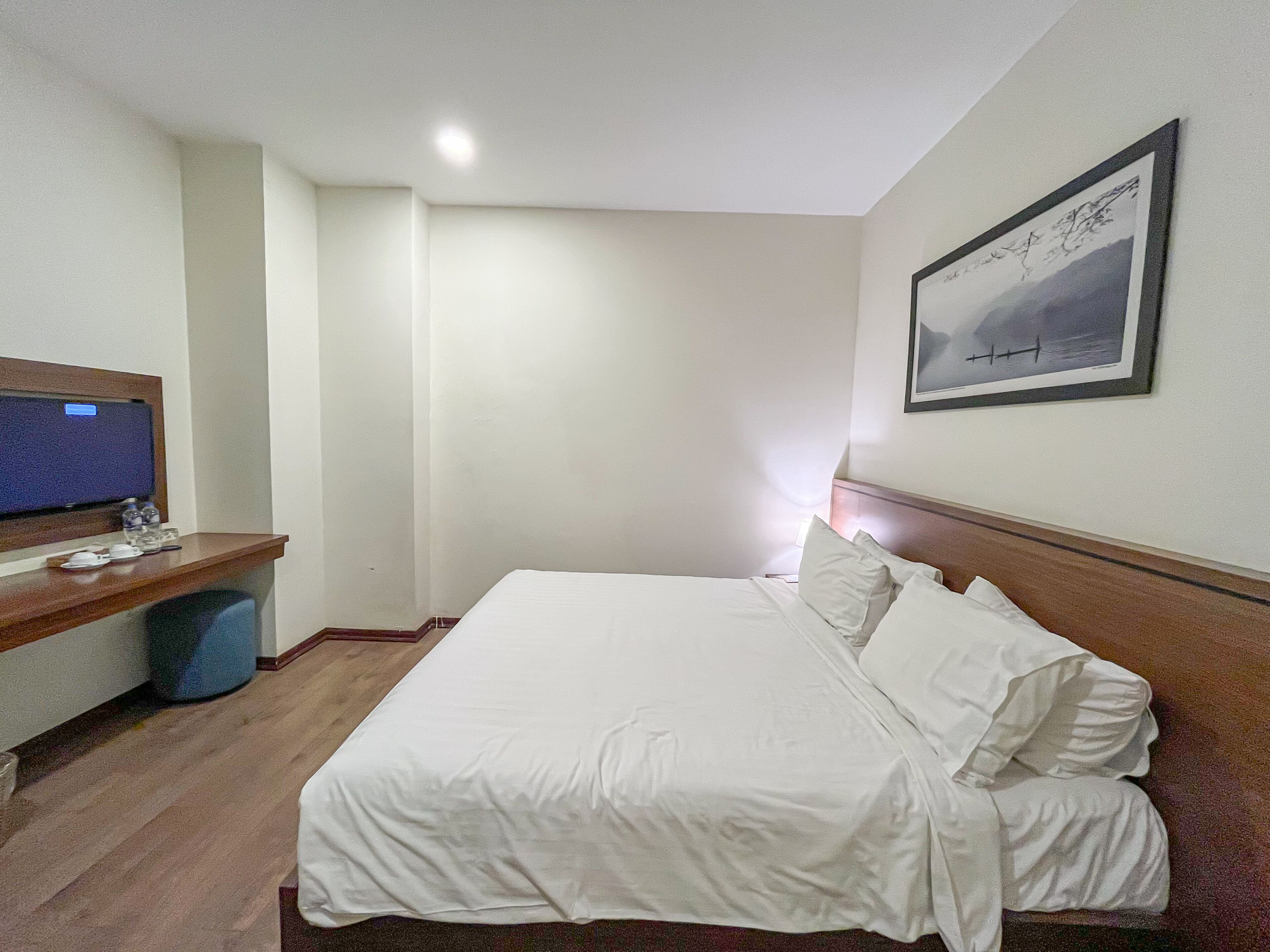 A hotel room with a bed, a desk with a computer, and a wall-mounted TV.