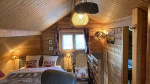 Acogedora habitación de cabaña de madera con cama, silla, mesita y ventana con cortinas.