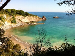 Un paysage côtier caractérisé par une plage de sable, des eaux turquoise et limpides, et des falaises rocheuses.