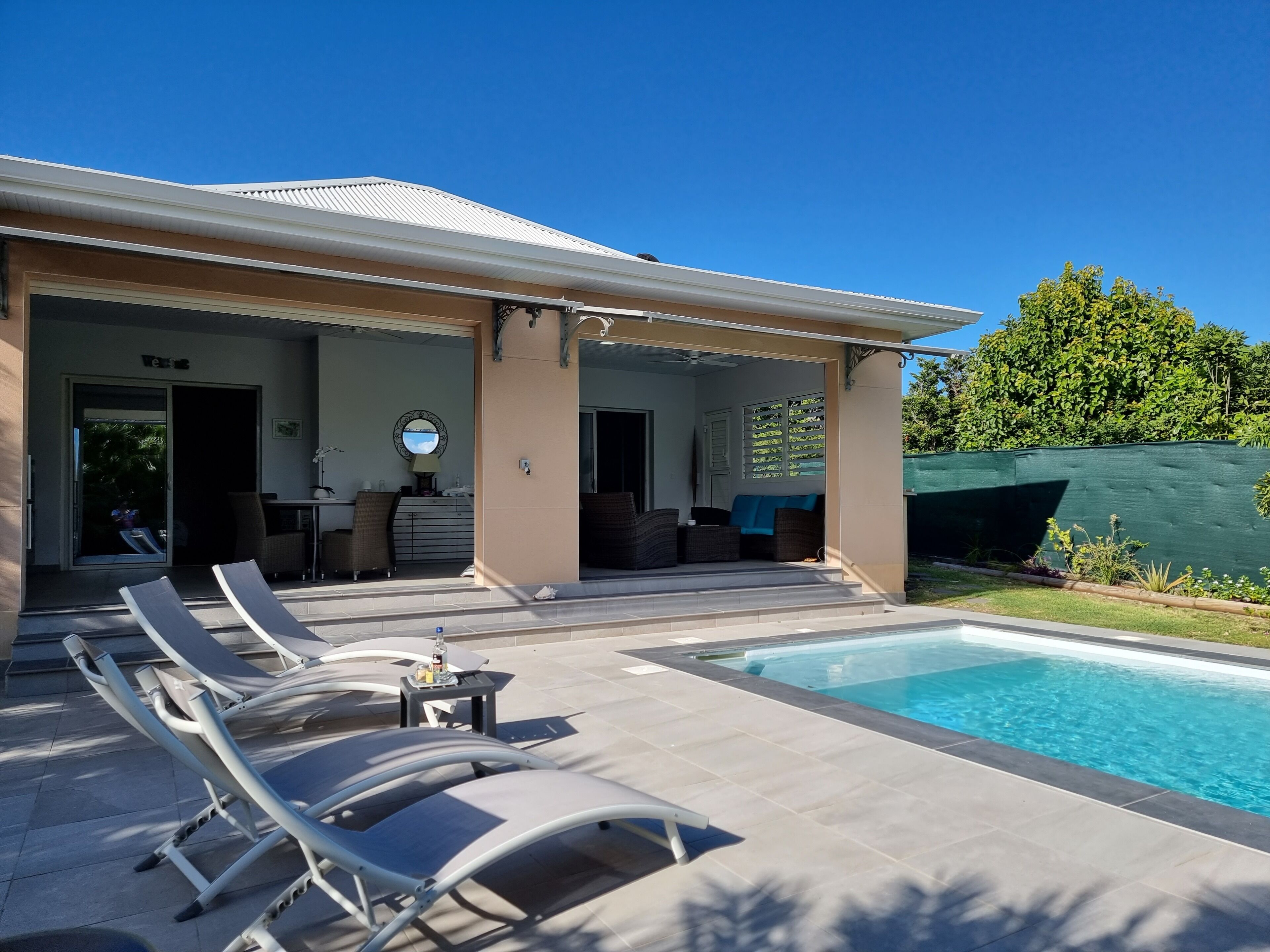 Ein modernes Haus mit Swimmingpool, Liegestühlen und einer überdachten Terrasse.