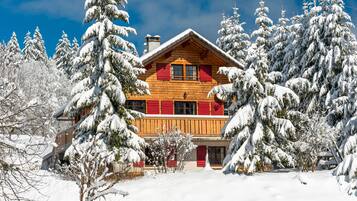 Une cabane en bois avec un toit rouge, entourée d’arbres couverts de neige.