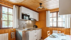 A compact kitchen with wooden walls, a stainless steel sink, and a dining table set for four. - T2 in chalet with terrace and private parking - Montagnes du Jura (Lamoura)