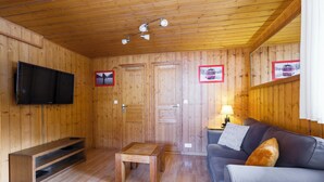 A wooden-paneled room with a flat-screen TV, a sofa, a coffee table, and two doors. - T2 in chalet with terrace and private parking - Montagnes du Jura (Lamoura)