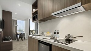 A modern kitchen with a built-in microwave, a coffee maker, and a sink. There is a dining area with a table and chairs visible in the background. - Quest Innaloo (Innaloo)